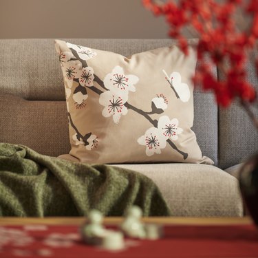 A beige floral pillow resting on a beige couch next to a green blanket.