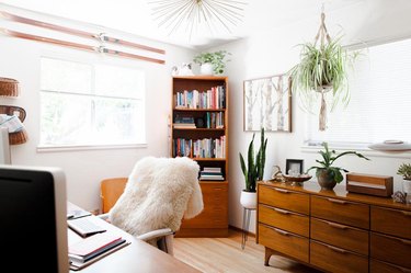 Office with wood furniture, plants, sheepskin throw, and Modernist accents.