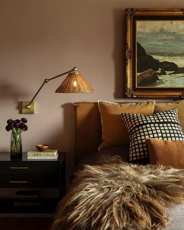 Bedroom in shades of mustard and blush with fur throw, woven lamp, and vase of flowers