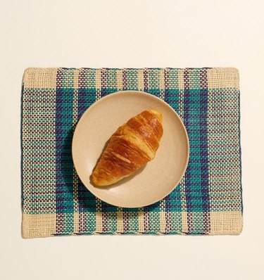 blue and cream patterned placemat with plate with croissant on top
