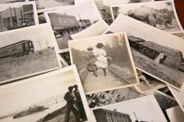 Black-and-white Polaroid photos from the 1920s through 1950s showing two people walking in dresses on train tracks, a train car, and other buildings and homes.