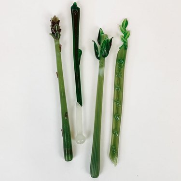 Four vintage handmade glass vegetable swizzle sticks for stirring drinks, including an asparagus, celery, snap pea, and green onion.