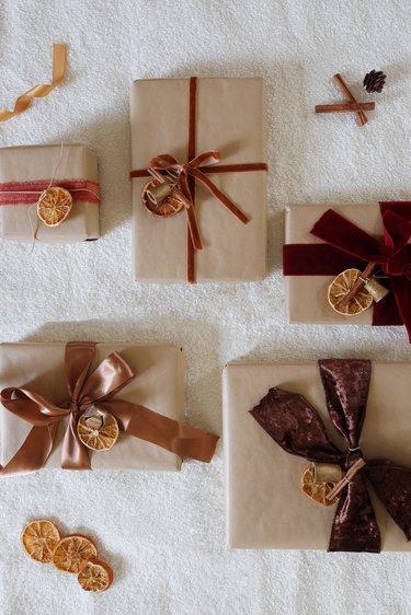 Dried orange gift toppers tied to five gifts wrapped with brown Kraft paper and velvet ribbon