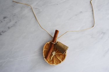 Dried orange slice and brass bell tied to cinnamon stick with leather cord