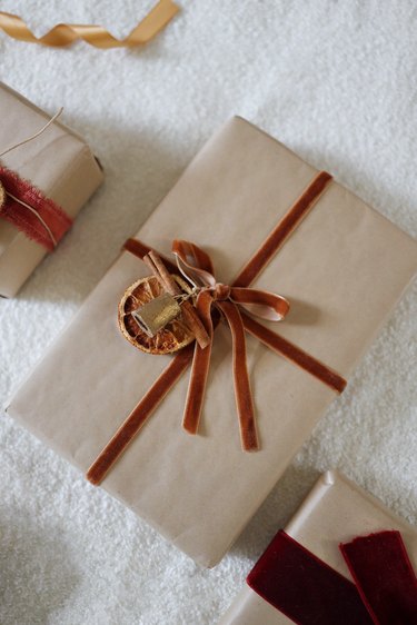Dried orange gift topper with cinnamon and brass bell tied to gift wrapped with brown Kraft paper and velvet ribbon