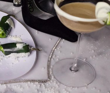 Jalapenos covered in chocolate on a white plate next to a martini glass and a black heel.