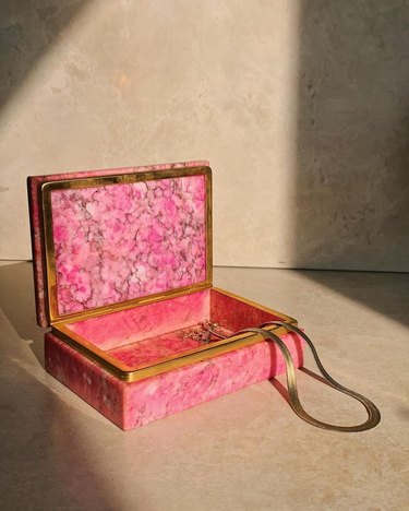 A pink alabaster jewelry box with gold trim and a gold necklace inside.
