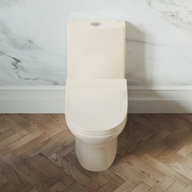 An ivory dual-flush toilet on a herringbone patterned floor, against a marbled wall