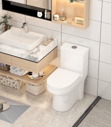 A white dual-flush toilet in a bathroom with floating shelves and large white tile on the walls