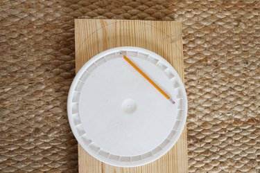 Tracing a rounded shape on the top of the wood board using a bucket lid as a template