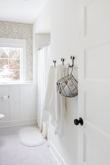 White bathroom with wall hooks and hanging basket.