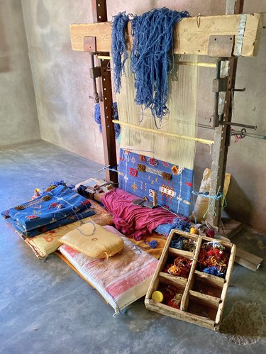 A loom showing a blue Moroccan rug with symbols on it in the making.