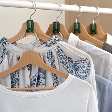 Clothes hanging on wood hangers in a closet, with green hanger connectors on the hanger handles being used to hang more clothing.