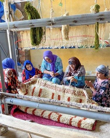 Amazigh praying around a Moroccan rug featuring a beige and red pattern.