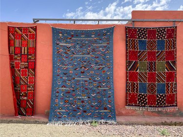 Three Moroccan rugs hanging off the side of a bright orange building.