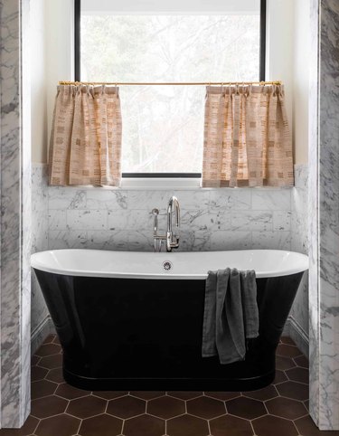 Black bath tub, maroon tile floors, curtains.