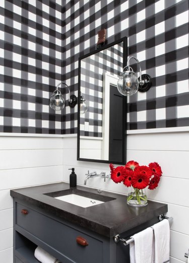 Bathroom with black and white checked wallpaper, black vanity.