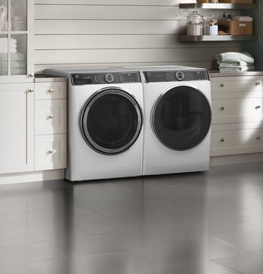 A white washer and dryer in a laundry room with concrete floors and shiplap walls