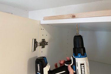 Drilling a pilot hole into scrap wood on top of IKEA PAX wardrobe