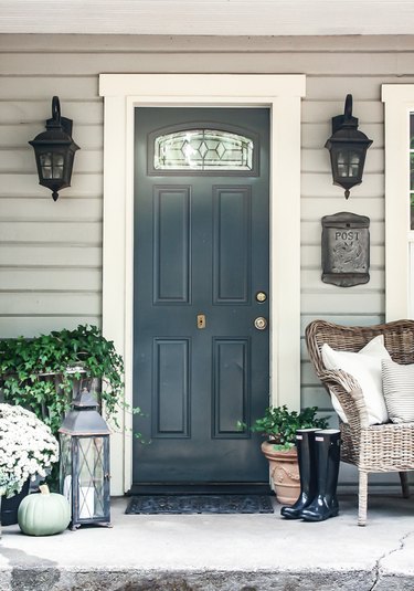 farmhouse style front porch with neutral door, plants and wicker chair