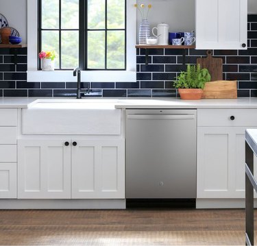A stainless steel dishwasher in a white kitchen that has a blue subway tile backsplash