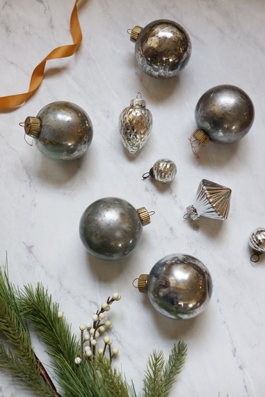 Several DIY mercury glass ornaments with sprig of pine and white berries and gold ribbon