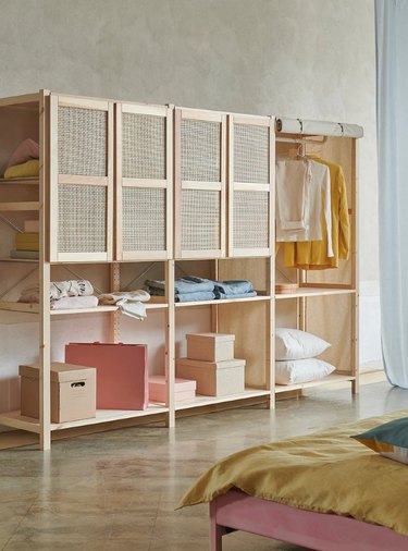 A wooden storage unit in a bedroom with clothes hanging and boxes stacked on shelves