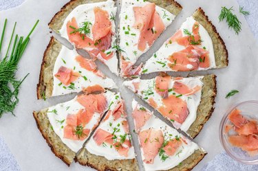An aerial view of the Smoked Salmon Latke Pizza surrounded by fresh dill, chives, and a small glass bowl filled with smoked salmon.