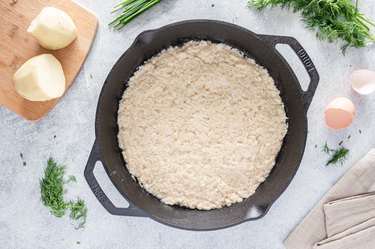 The potato mixture spread in an even layer inside a black cast iron skillet.