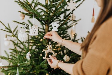 person placing rocking horse ornament on christmas tree