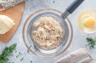 The potato grated inside a small colander over a small glass bowl.