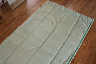 Sage green velvet curtain panel laid flat on floor with green rick rack trim along the side
