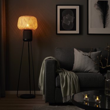 The IKEA floor lamp speaker in a darkened living room with the lamp's light giving off a soft glow.