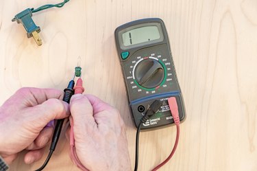 testing string light bulb with multimeter electric tester, wood background