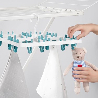 A clothes hanger with 24 blue clothespins, some of which are holding wet napkins and a teddy bear.