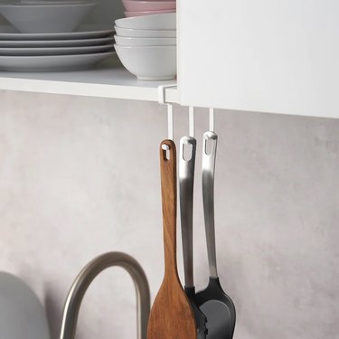 A white hook rack holding spatulas underneath a white upper kitchen cabinet.