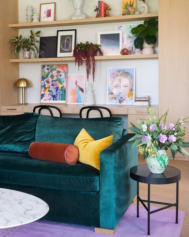 Living room with teal velvet sofa, yellow and caramel pillows, with a gallery wall in the background.