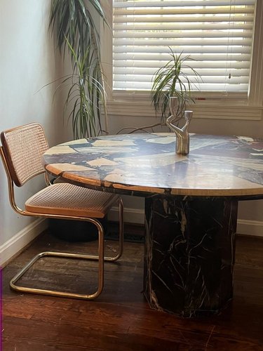 A beige and black vintage terrazzo dining table paired with an armless rattan dining chair.