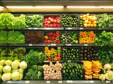 Photo of produce aisle at the grocery store including colored bell peppers, broccoli, eggplant, cucumbers, iceberg lettuce, and leafy greens.
