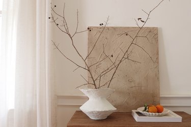 DIY paper mache vase with dried branches on cabinet next to bowl of oranges