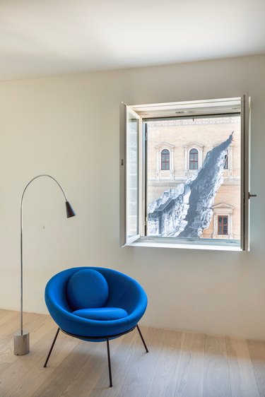 A blue bowl chair in a room with a window and lamp