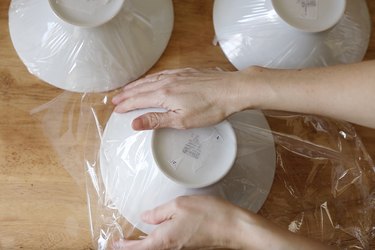 Wrapping three ceramic bowls with plastic wrap