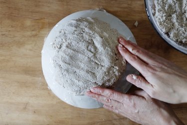 Pressing paper mache dough to back of plastic-covered bowl