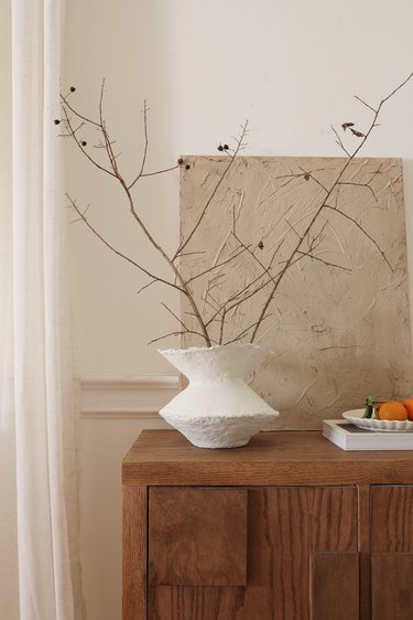 DIY paper mache vase with dried branches on cabinet next to bowl of oranges