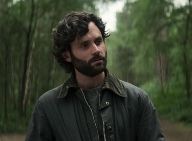 Joe Goldberg from 'You' season four in the woods wearing a dark jacket.