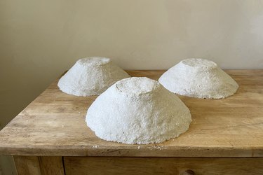 Three bowls with paper mache applied to them drying on wood table