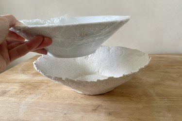 Removing plastic-covered ceramic bowl mold from paper mache bowl