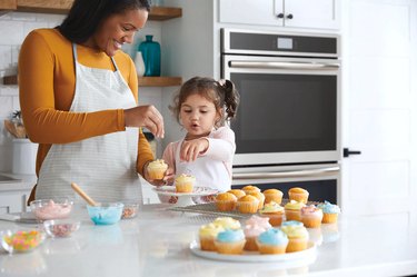 adult and child putting sprinkled on cupcakes near wall oven