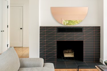 The fireplace featuring salmon-pink grout and a custom tinted mirror in a half-circle shape