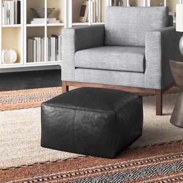 black leather pouf at foot of gray chair